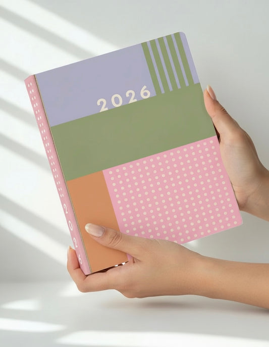 Hand holding a colorful planner with '2026' on a light background